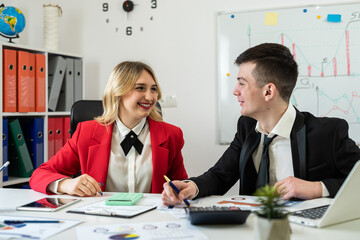 Two financial analysts working together with paper charts and laptops at office