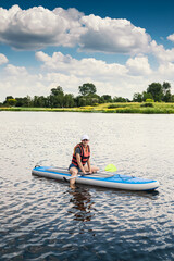 Fototapeta na wymiar Young pretty woman in orange life vests surfs on supboard in city lake