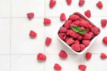 Bowl with fresh raspberry and mint on light tile background, closeup