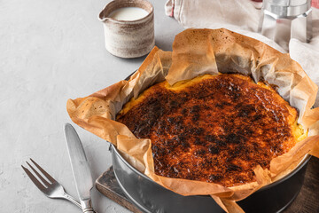Whole basque burnt cheesecake San Sebastian in baking dish with cream and cutlery on concrete table