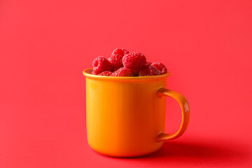 Cup with fresh raspberries on red background