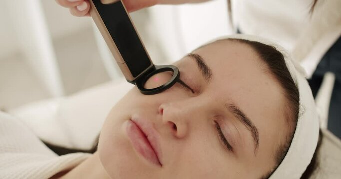 Close up of a young woman getting laser face treatment in a medical center, skin rejuvenation concept. Beautician cosmetologist doing procedure fractional microneedle. Beauty treatment.
