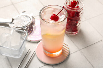 Glass of tasty cocktail with maraschino cherry on white tile background