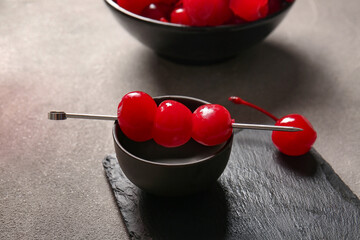 Bowl of tasty maraschino cherries on grey background