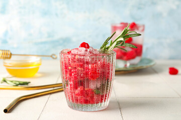 Glass of fresh raspberry lemonade and bowl with honey on white tile table