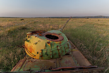 Destroyed rusted, abandoned and buned out battle tank in the green fields at sunset time. You can...