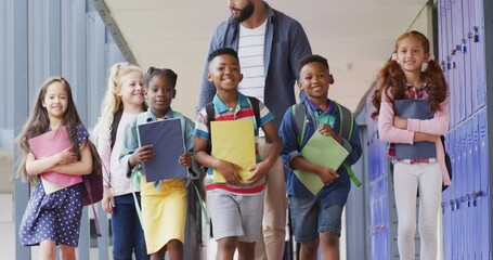 Diverse male teacher and happy schoolchildren walking at school - Powered by Adobe