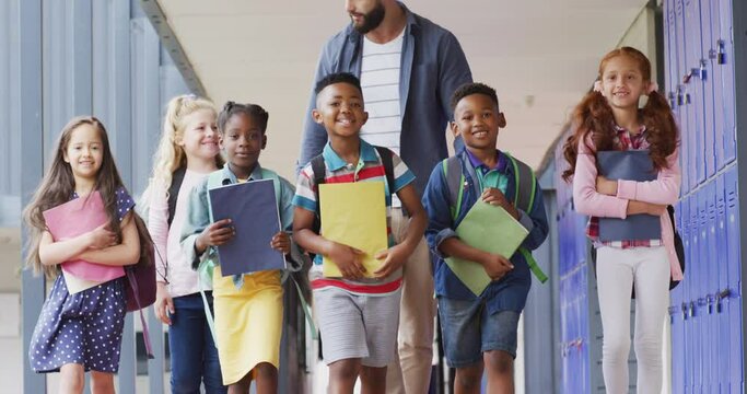 Diverse male teacher and happy schoolchildren walking at school