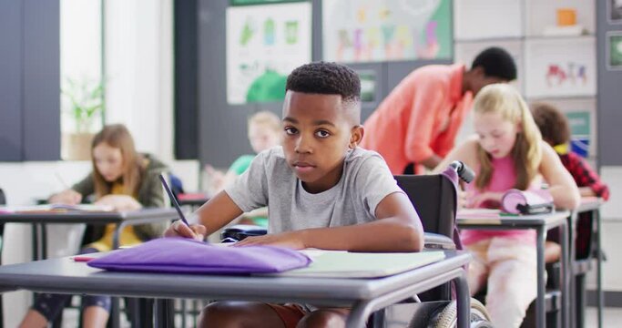 Portrait of happy diverse schoolchildren at desks writing in school classroom