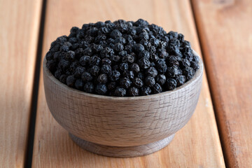 Black peppercorns in wooden bowl on table