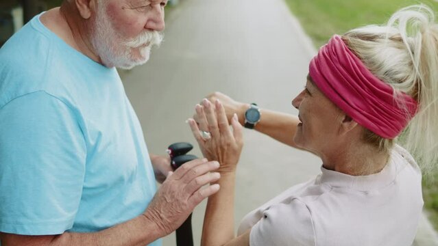Mature 50s woman tapping touchscreen on smart watch, tracking distance, checking pulse and teaching her retired old friend ohow to use smart watch