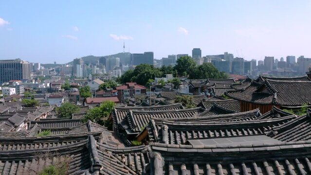 한국 서울 북촌한옥마을을 드론으로 낮은 고도에서 전진하며 촬영, 맑은 하늘과 남산, 서울의 전경이 멀리 보인다