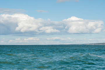 View of the sea with the coast in the distance. Calm waves with a blue cloudy sky in warm, summer weather.