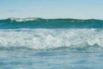 View of seawater with focus on the crest of a wave. Blurred background with low depth of field. Template on the theme of a seaside vacation with blank space for text.