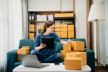 Caucasian young woman SME working using smartphone or tablet taking receive and checking online purchase shopping order to freelance online concept.