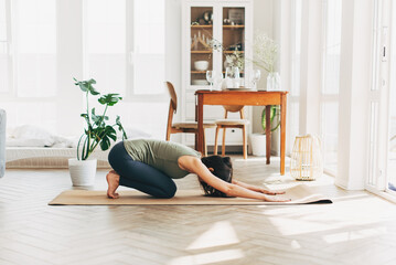 Joyful young lady in sportswear planking in living room, watching fitness video or having video conference with fitness trainer, sporty woman exercising and watching at smartphone screen, free space