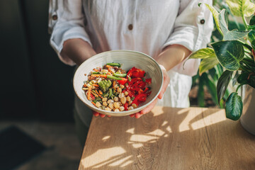 Young woman eating healthy food sitting in the beautiful interior with green flowers on the...
