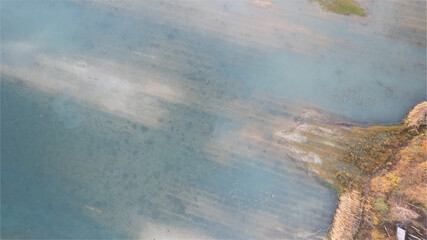 A stunning top-down aerial view of a serene forest lake's waterside during the fall. The vibrant autumn colors dance on the water's surface, presenting a breathtaking display of the season's palette
