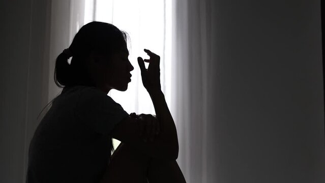 Silhouette of a sad  woman sitting in the dark room. Stress, violence, Domestic violence, family problems,  The concept of depression and suicide.