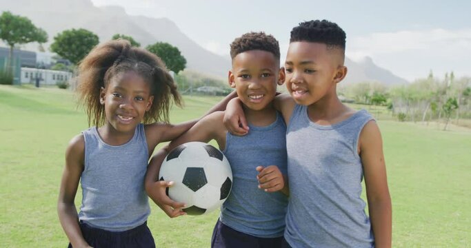 Video portrait of three happy african american children holding football in school field