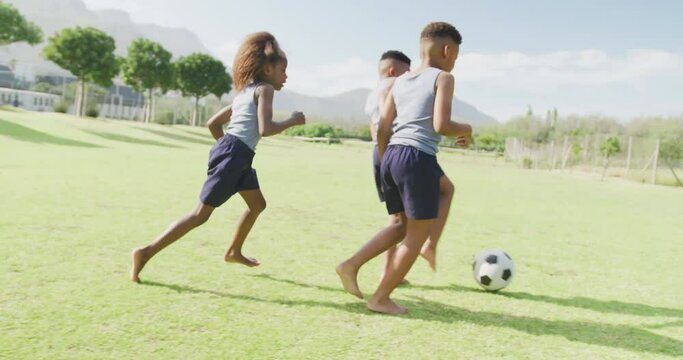 Video of three african american schoolchildren playing football barefoot in field