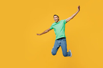 Fototapeta na wymiar Full body young man of African American ethnicity he wears casual clothes green t-shirt hat jump high with outstretched hands pov flying isolated on plain yellow background studio. Lifestyle concept.