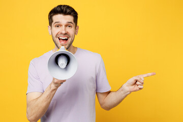 Young man wears light purple t-shirt casual clothes hold in hand megaphone scream announces discounts sale Hurry up point aside isolated on plain yellow background studio portrait. Lifestyle concept. - obrazy, fototapety, plakaty