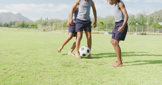 Video of three happy african american schoolchildren playing football barefoot in field
