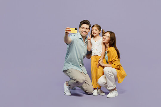Full body young happy parent mom dad with child kid daughter girl 6 year old wear blue yellow casual clothes do selfie shot on mobile cell phone isolated on plain purple background Family day concept