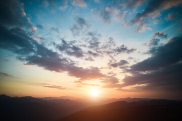 Panoramic view of bright evening sun and dramatic cloudy sky over mountains. Magnificent scenery of mountain hills under colorful evening sky with clouds and setting sun. Beauty of nature concept.