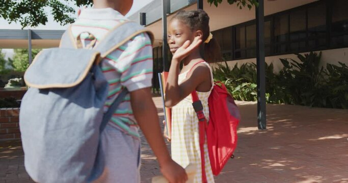 Video of happy african american boy and girl with schoolbags high fiving outside school