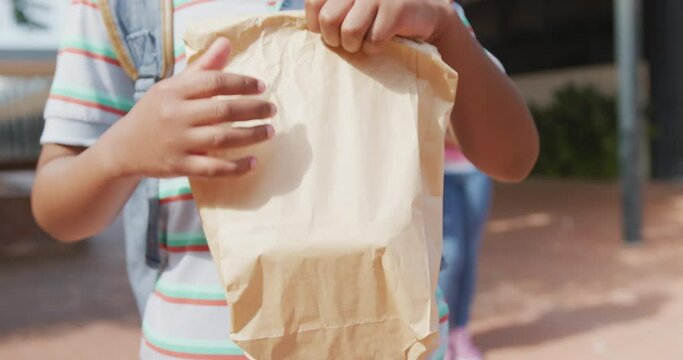 Video midsection of african american schoolboy holding packed lunch outside school