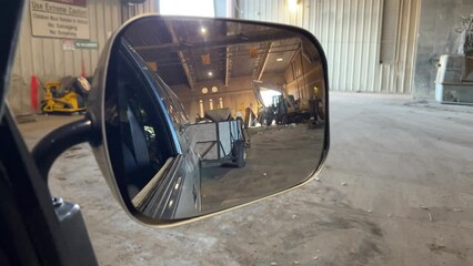 Looking through a mirror of a truck as it backs up a trailer full of junk at the dump you can also see some large industrial vehicles in the background