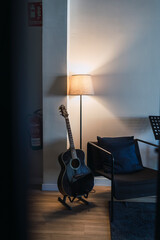 guitarra acústica en soporte junto a sillón y lampara encendida