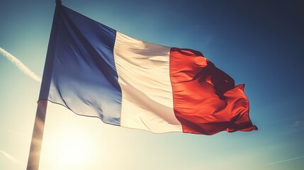 French flag waving in the wind on blue sky background with sun flare. Big Flag of France on a sunny beautiful bright summer day. French flag waving in the wind. .