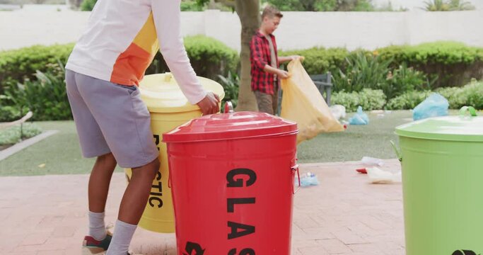 Video of two happy diverse schoolboys collecting rubbish for recycling in schoolyard