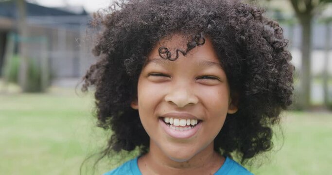 Video portrait of smiling biracial schoolgirl in school playing field, with copy space