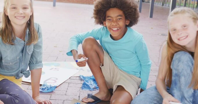 Video portrait of happy diverse schoolchildren making protest placards in schoolyard, copy space