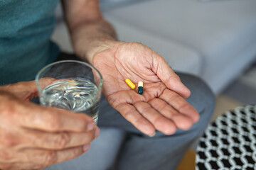 A senior man, feeling stressed and depressed, takes a pill with a glass of water. Depicting the act of self-medication and the impact of antidepressant drugs, use of medicines