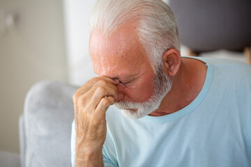 Tired, depressed senior man sitting on couch in living room feeling hurt and lonely. Aged,...