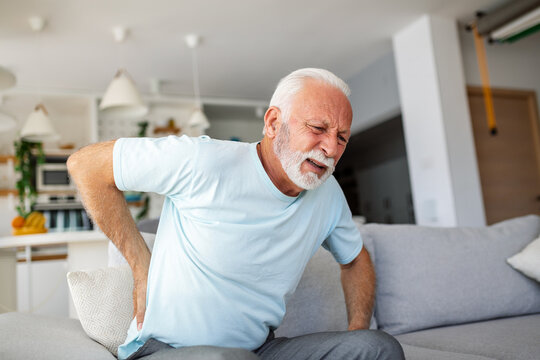 Senior man, with back pain, touches his back, illustrating sciatica and sedentary lifestyle. Emphasizing spine health and the significance of healthcare and insurance in this stock image.