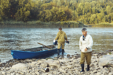 Two men early in the morning on the river prepare the boat for morning fishing. Rocky river bank. High quality photo
