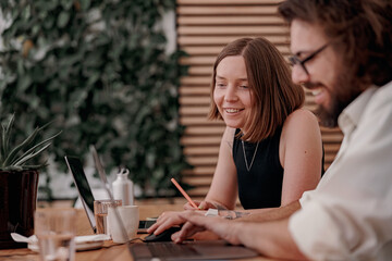 Two smiling colleagues working together on project while sitting on the desk in cozy coworking