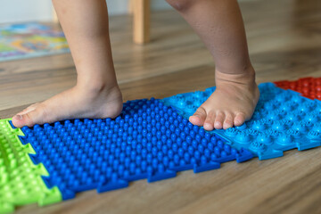 children's feet, stepping on colorful massage mats with different textures for foot massage, .Exercises for legs orthopedic massage carpet.