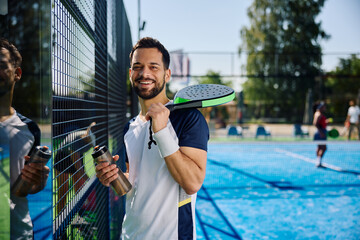 Happy man having water break during paddle tennis match and looking at camera.
