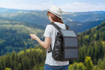 Young woman with mobile phone in hands connected to backpack with portable solar battery
