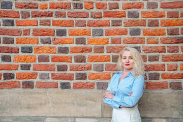 Fototapeta na wymiar a successful business woman stands near a red brick wall on the street. a woman dressed in white trousers and a blue shirt. copy space.