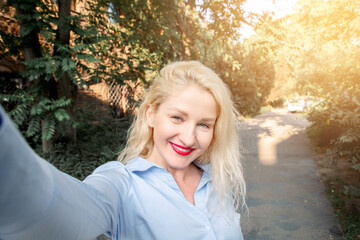 Happy girl with blonde hair dressed in wearing a blue shirt, walking around the city, posing for selfies. a warm summer evening.