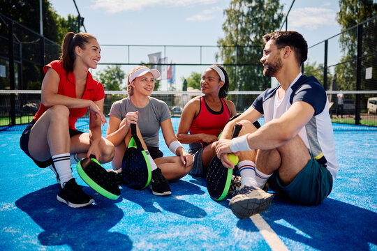 Group of athletic friends talk while relaxing after playing paddle tennis on outdoor court. - Powered by Adobe
