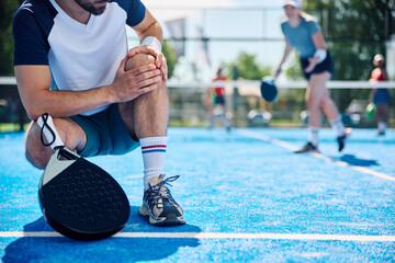Close up of athlete feels pain in his knee while playing padel on outdoor tennis court.
